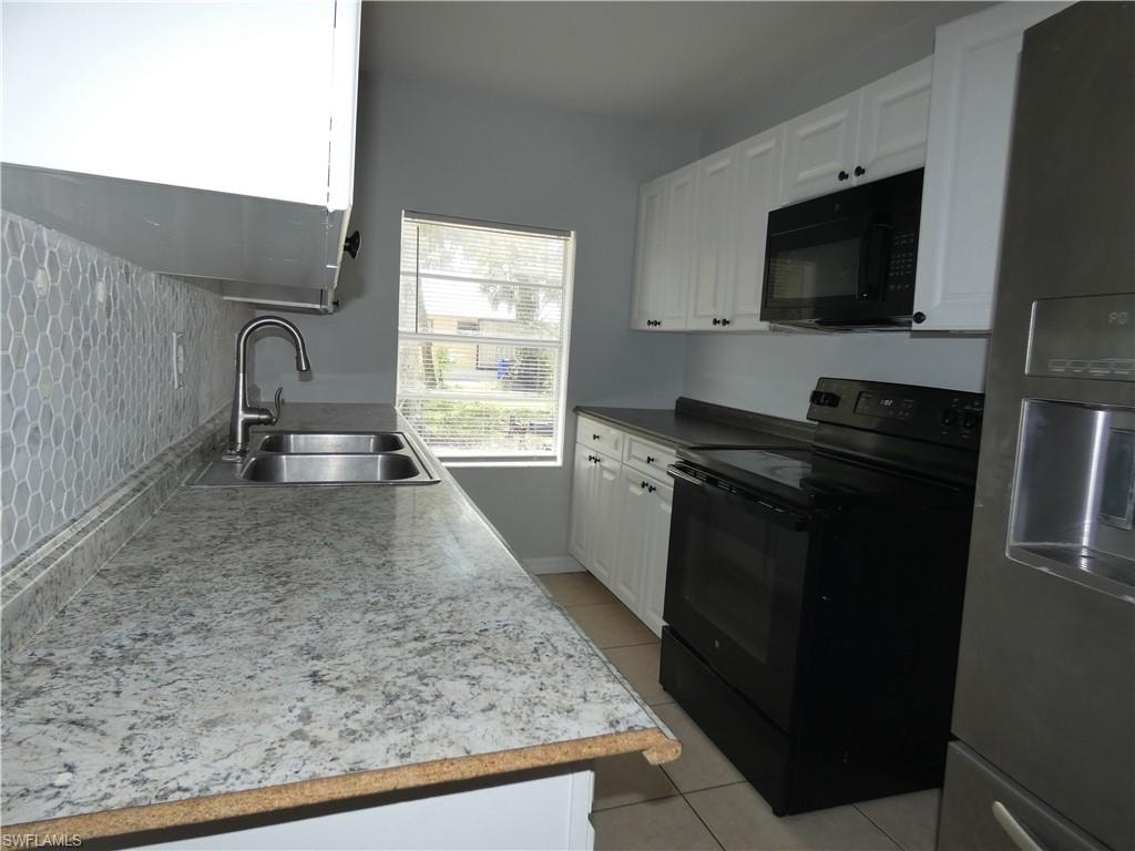 Kitchen with black appliances, a sink, light tile patterned floors, white cabinetry, and backsplash