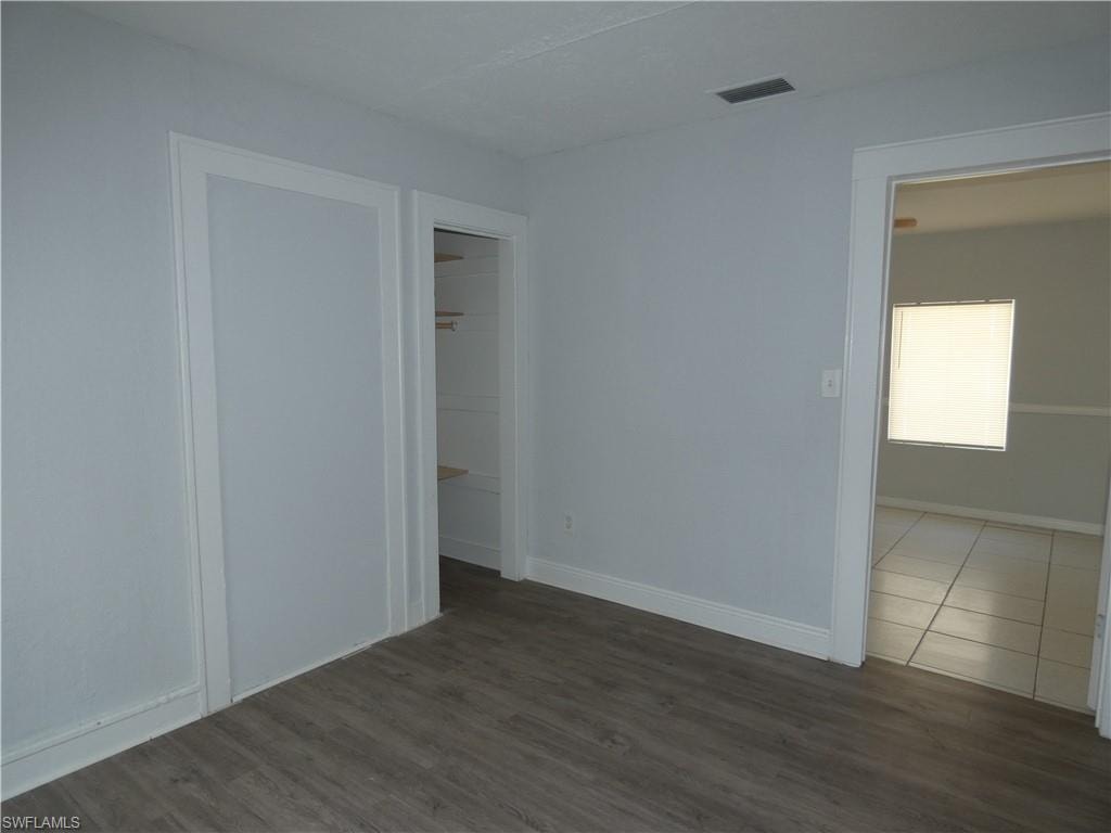 Unfurnished bedroom with wood finished floors, a walk in closet, and baseboards