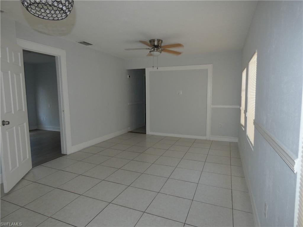 Empty room with a ceiling fan, light tile patterned flooring, and baseboards