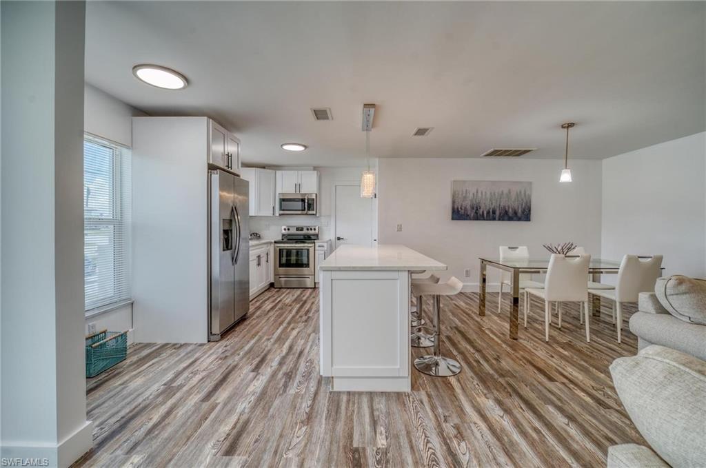 Kitchen featuring stainless steel appliances, a breakfast bar area, light wood-style floors, light countertops, and white cabinetry