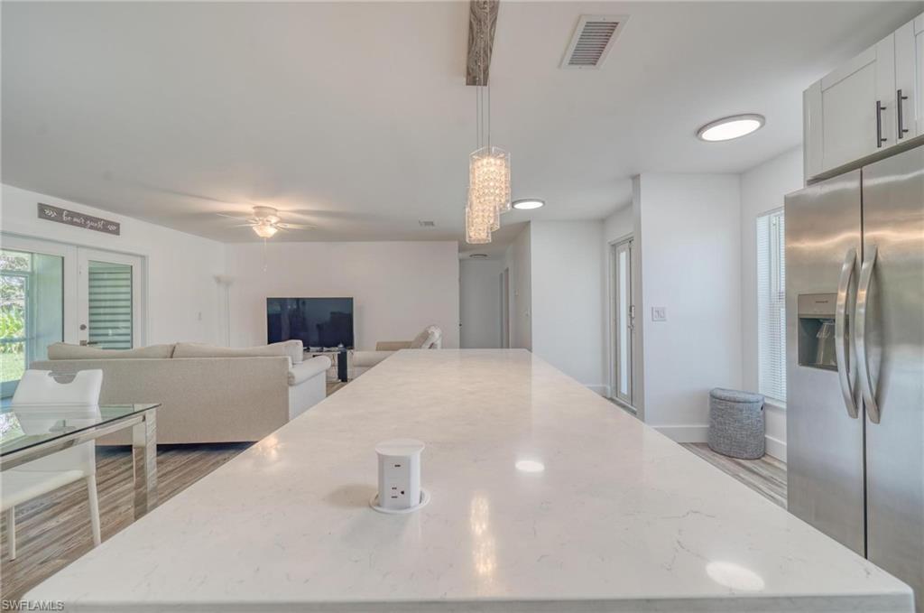 Kitchen featuring stainless steel refrigerator with ice dispenser, a center island, decorative light fixtures, ceiling fan, and light stone countertops