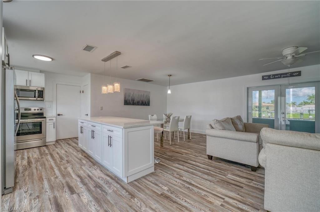 Kitchen featuring stainless steel appliances, open floor plan, light wood-style floors, white cabinets, and light countertops