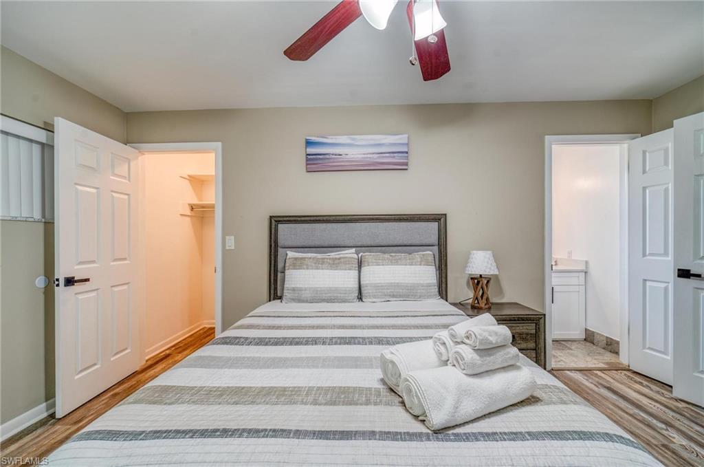 Bedroom featuring wood finished floors, ensuite bathroom, a walk in closet, a ceiling fan, and baseboards