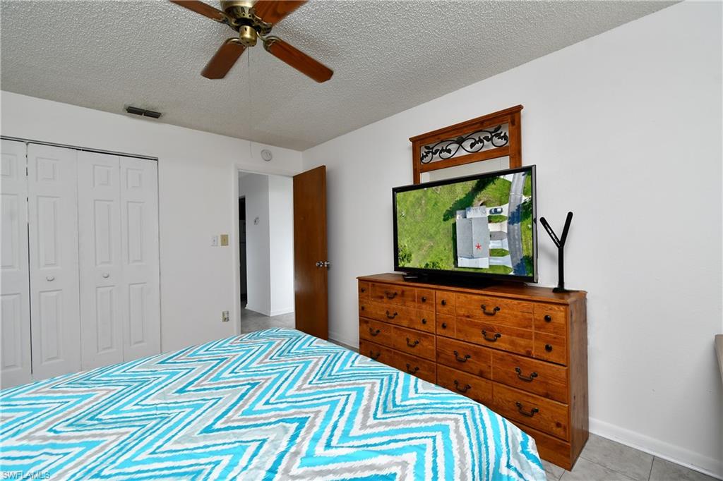 Bedroom with a textured ceiling, a closet, ceiling fan, tile patterned floors, and baseboards