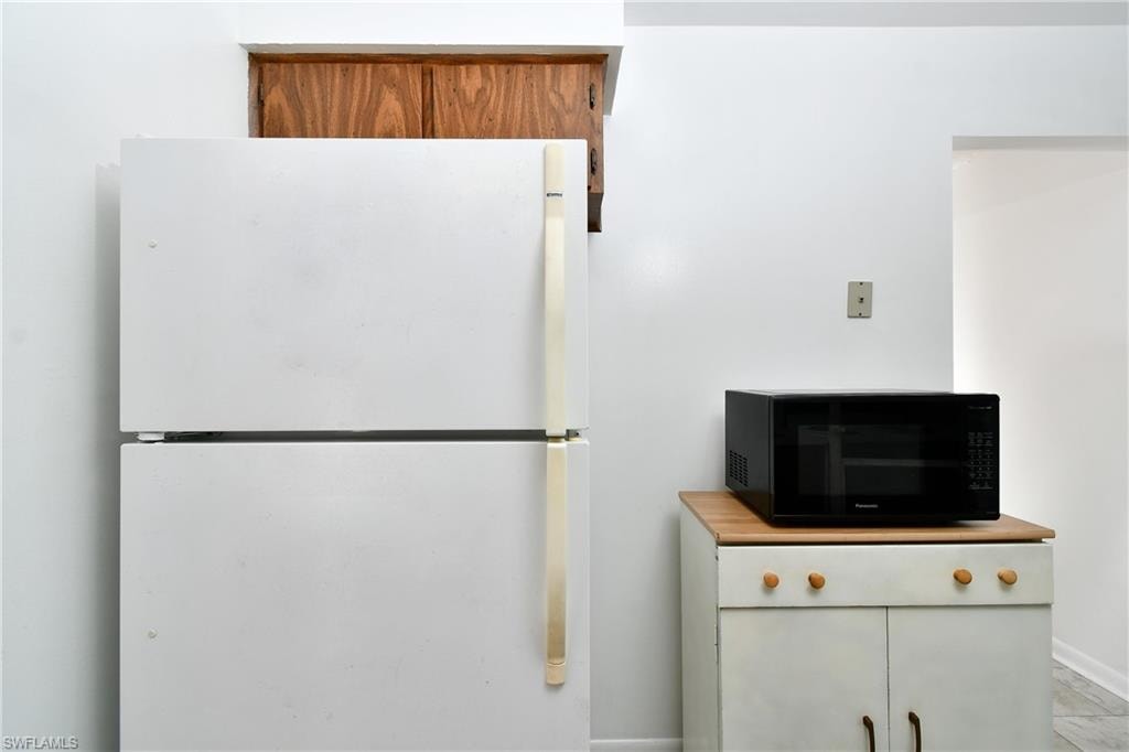 Kitchen view of black microwave, freestanding refrigerator, and baseboards