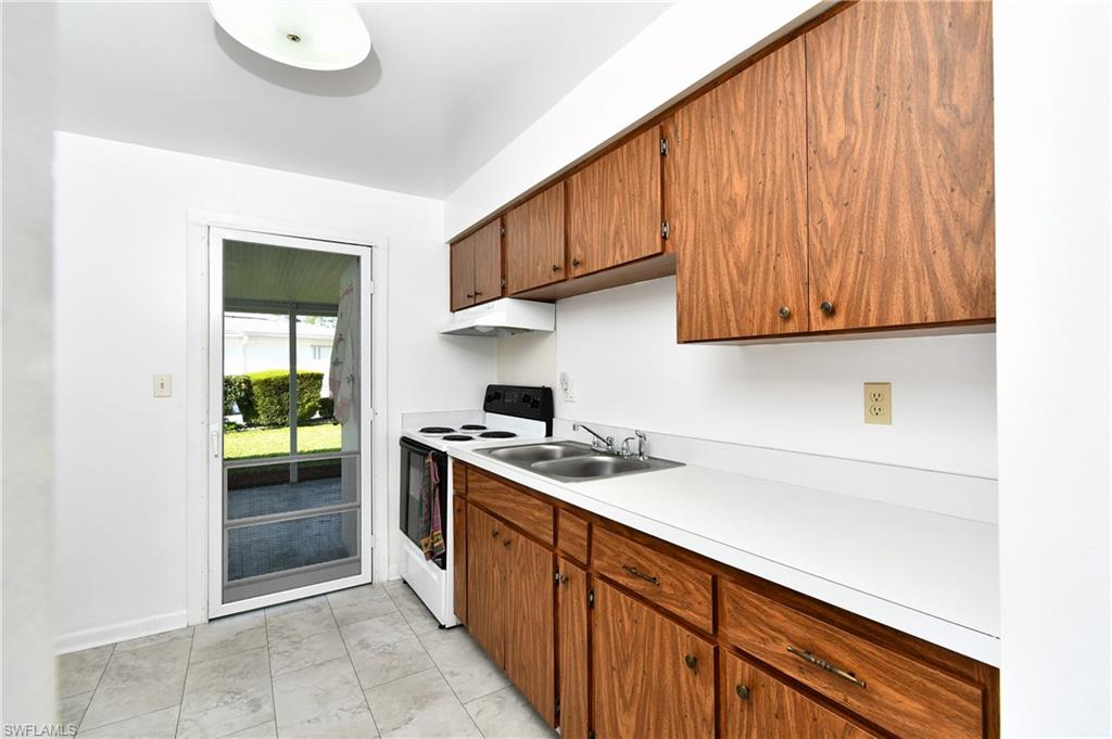Kitchen featuring white electric range oven, a sink, light countertops, brown cabinets, and baseboards