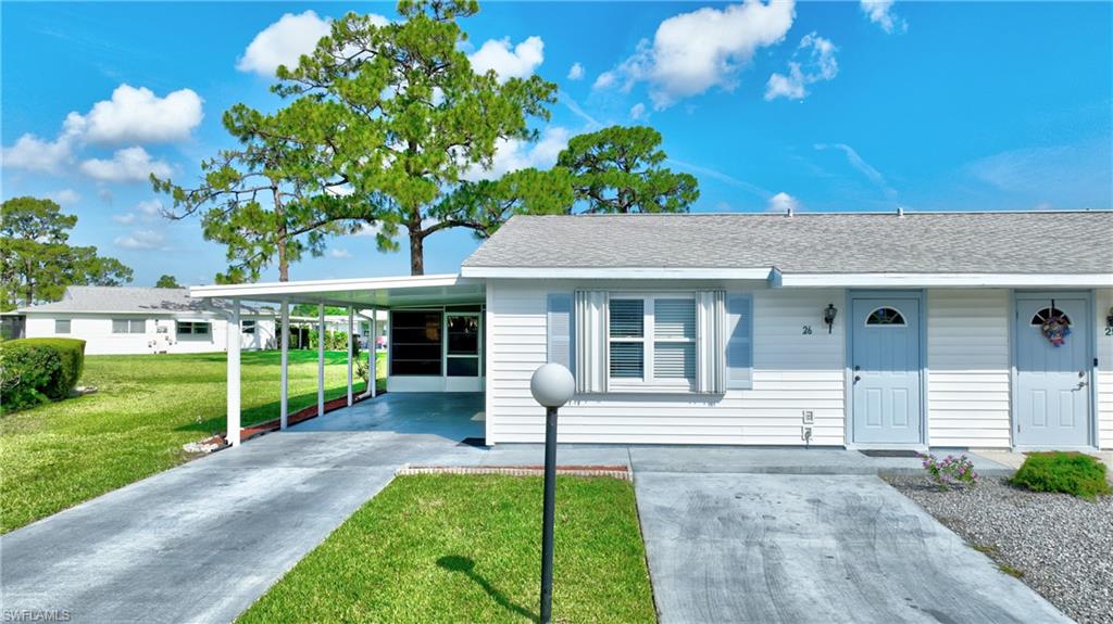 View of front facade with concrete driveway, a front lawn, a carport, and roof with shingles