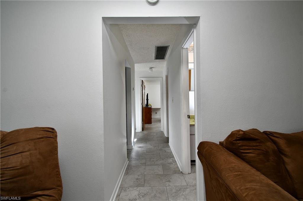 Corridor with baseboards and a textured ceiling