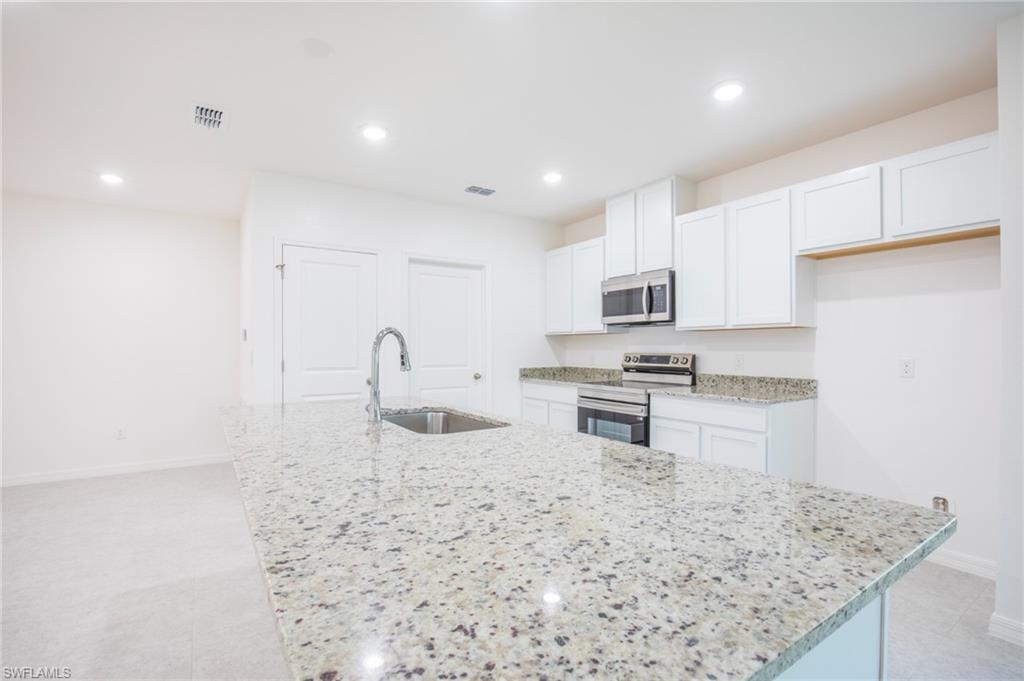 Kitchen with stainless steel appliances, white cabinetry, an island with sink, recessed lighting, and light stone countertops