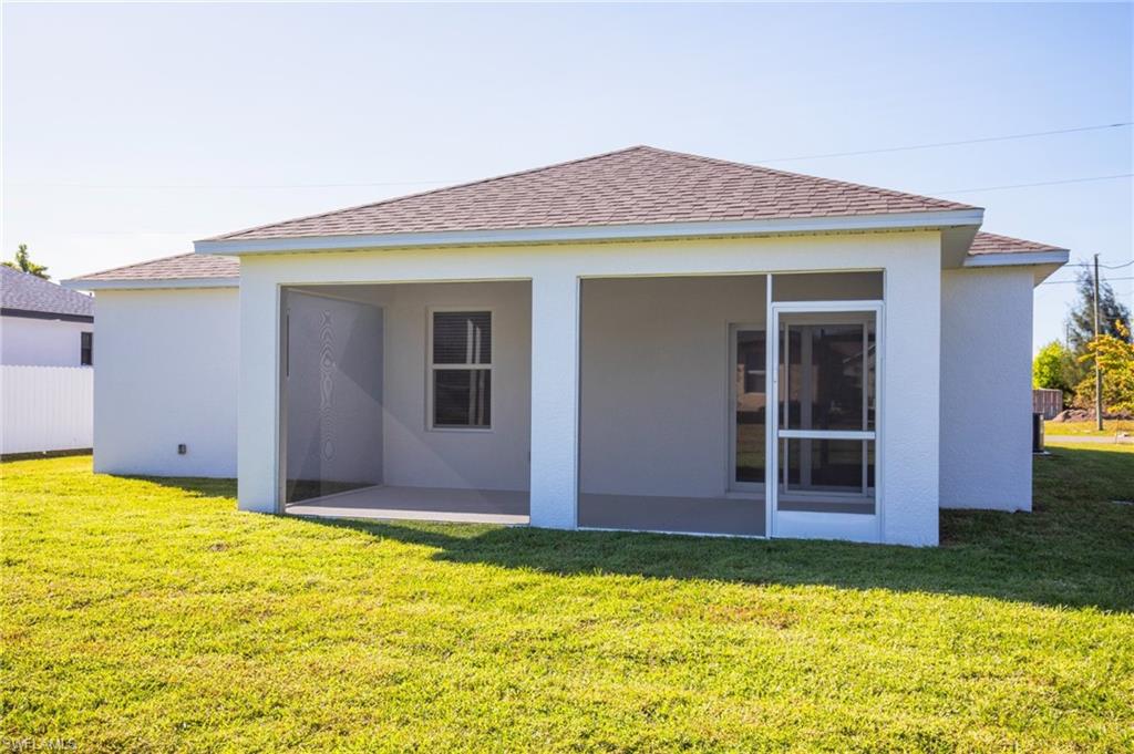 Back of property featuring roof with shingles, stucco siding, and a yard