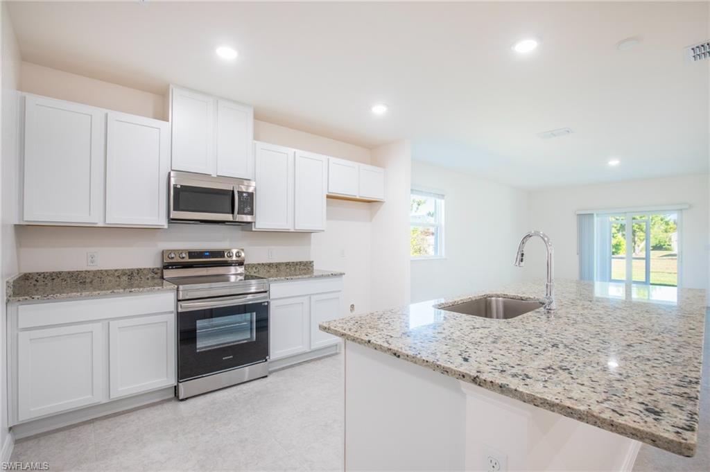 Kitchen featuring stainless steel appliances, light stone counters, white cabinets, recessed lighting, and a center island with sink