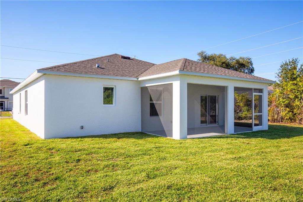 Back of property with a lawn, roof with shingles, and stucco siding