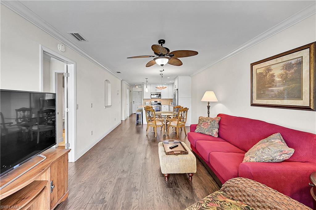 Living room with wood finished floors, ceiling fan, ornamental molding, and baseboards