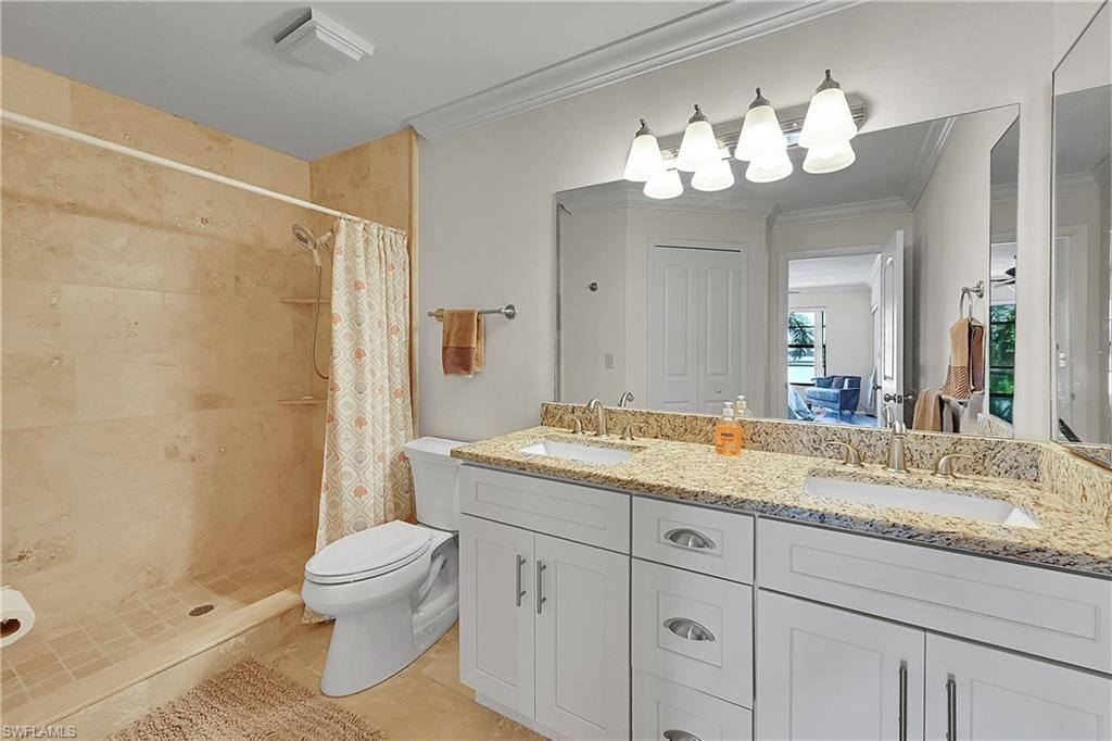 Bathroom featuring crown molding, toilet, double vanity, tiled shower, and tile patterned floors