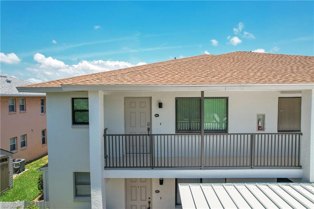 View of front entry with roof with shingles, stucco siding, cooling unit, and a balcony