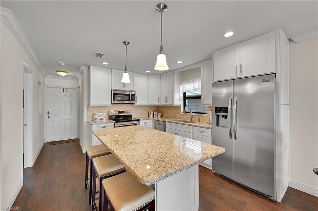 Kitchen featuring appliances with stainless steel finishes, a sink, light stone counters, crown molding, and kitchen island