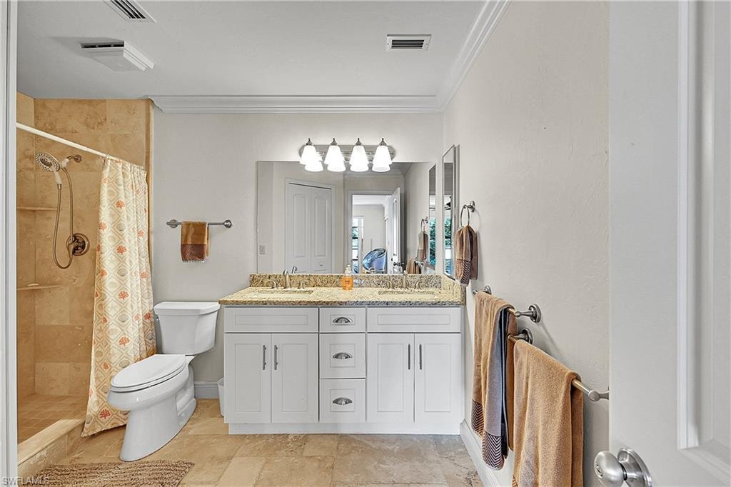 Full bathroom with toilet, double vanity, tiled shower, and crown molding