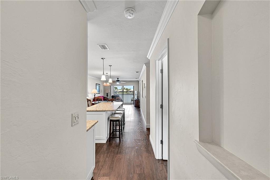 Corridor with crown molding, wood-style floors, baseboards, and a textured wall