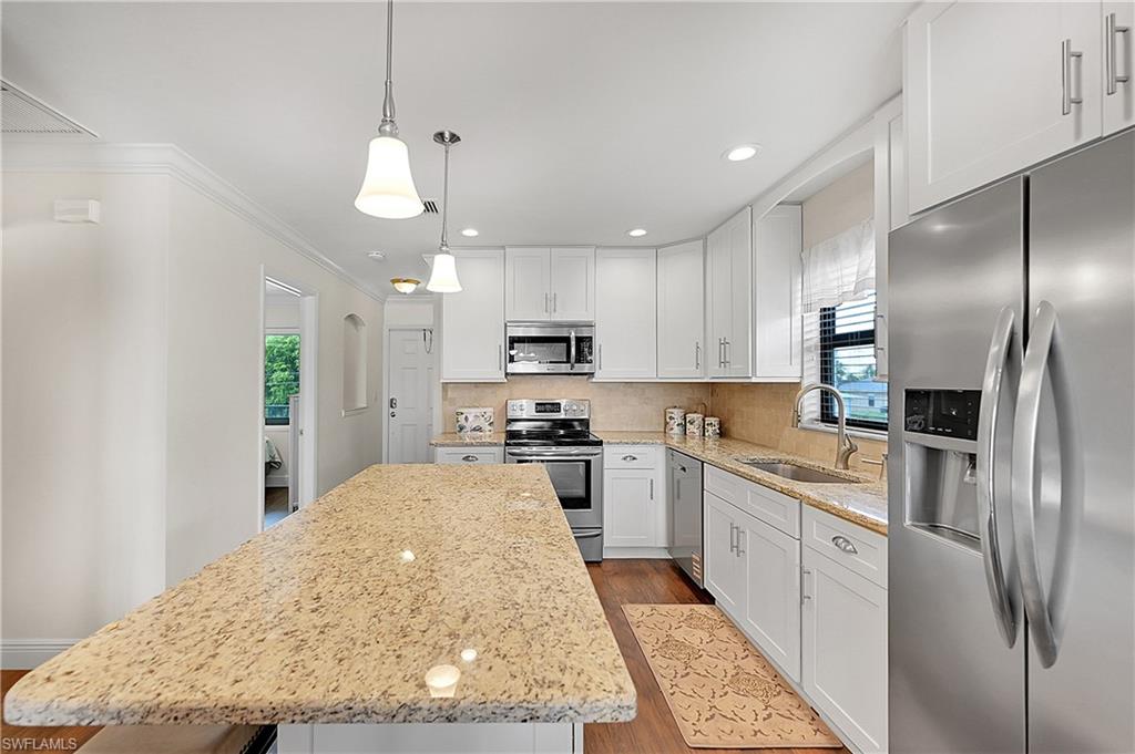 Kitchen featuring appliances with stainless steel finishes, a sink, a kitchen island, wood finished floors, and white cabinets