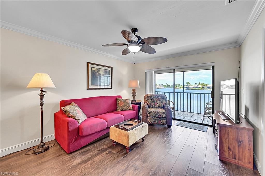 Living area featuring wood finished floors, a ceiling fan, crown molding, and baseboards