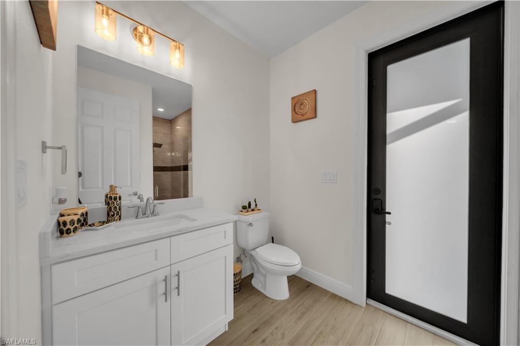 Full bathroom featuring tiled shower, vanity, baseboards, toilet, and wood finished floors