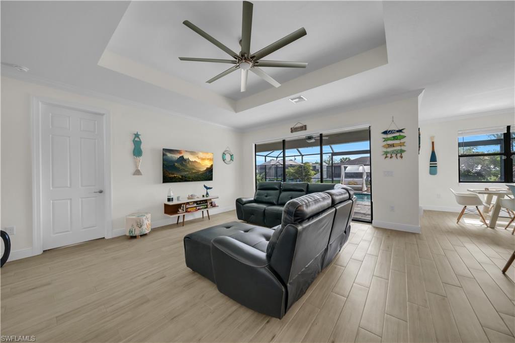 Living room featuring a tray ceiling, plenty of natural light, light wood-style flooring, and ornamental molding