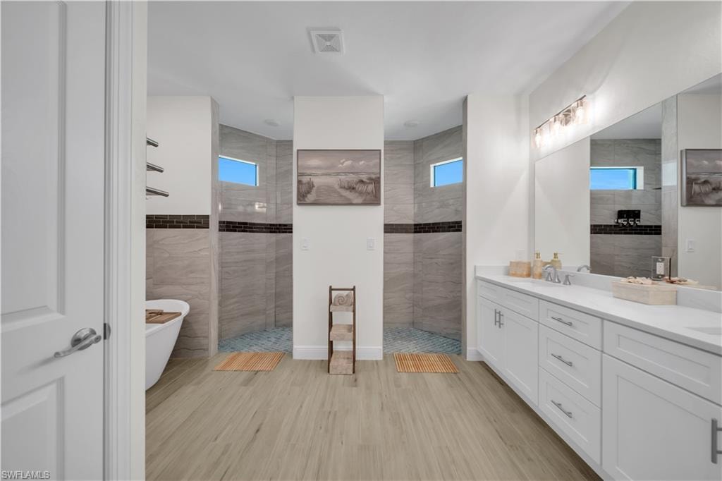Full bath with tile walls, walk in shower, double vanity, healthy amount of natural light, and a freestanding tub