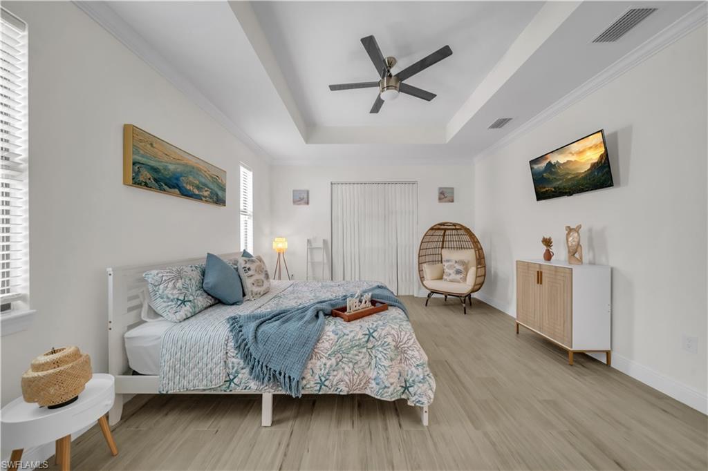 Bedroom with light wood-style flooring, a raised ceiling, a ceiling fan, baseboards, and crown molding
