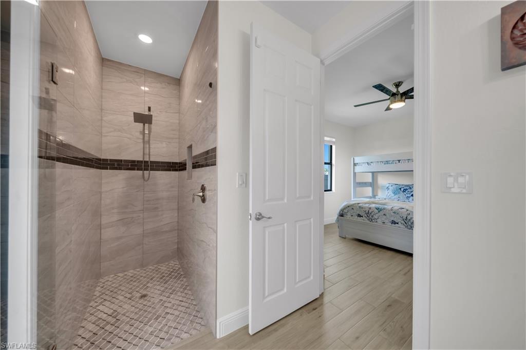 Ensuite bathroom with tiled shower, wood finished floors, ceiling fan, baseboards, and recessed lighting