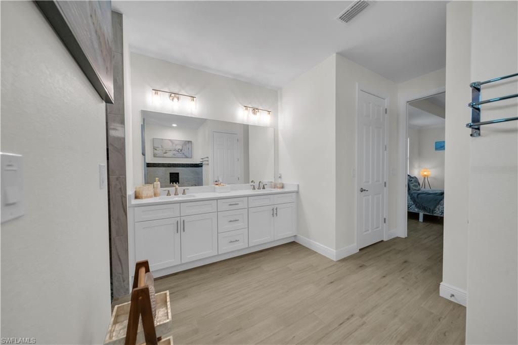 Bathroom with connected bathroom, double vanity, wood finished floors, and baseboards