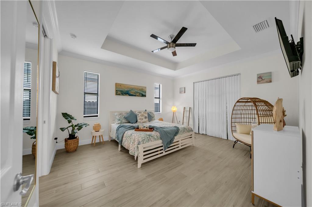 Bedroom with a raised ceiling, light wood-style floors, a ceiling fan, baseboards, and ornamental molding