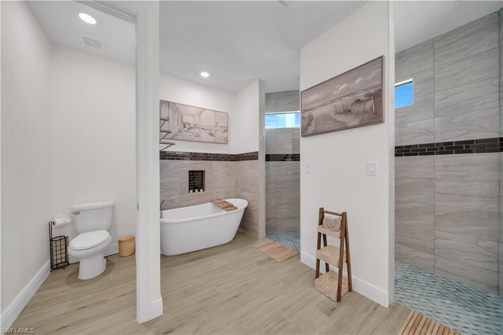 Bathroom featuring a fireplace, a freestanding tub, walk in shower, toilet, and wood finished floors