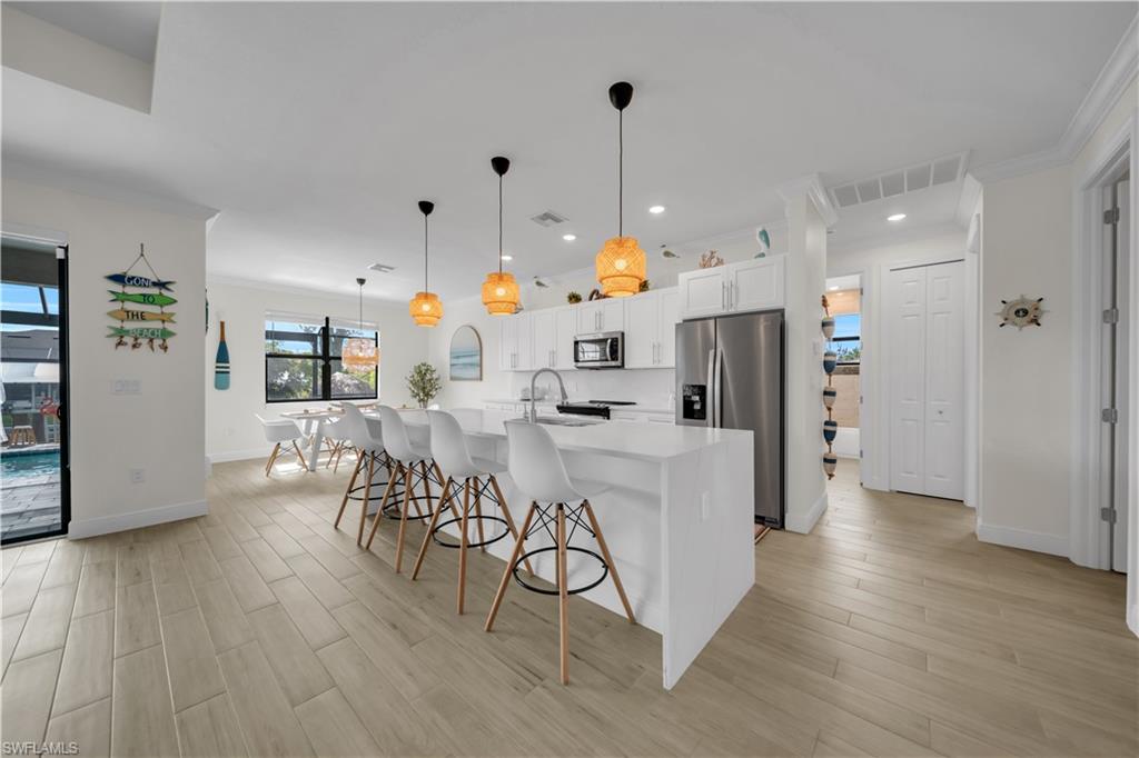 Kitchen with stainless steel appliances, a breakfast bar, white cabinets, light wood-style flooring, and recessed lighting