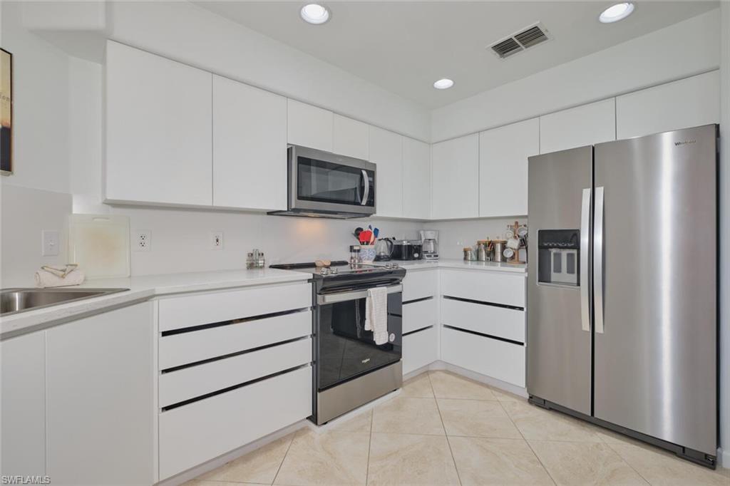 Kitchen with appliances with stainless steel finishes, light countertops, white cabinetry, a sink, and light tile patterned floors