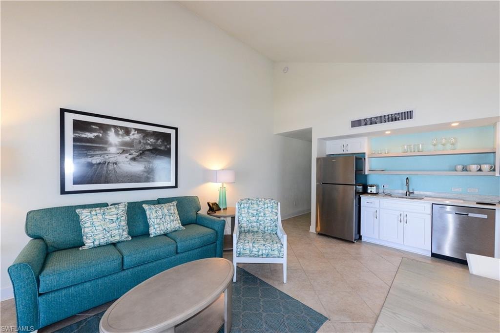 Living room with high vaulted ceiling, bar with sink, and light tile patterned floors