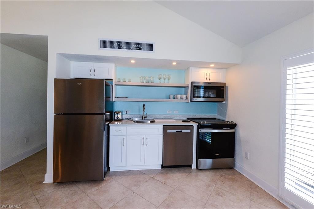 Kitchen featuring stainless steel appliances, a sink, vaulted ceiling, white cabinets, and light countertops