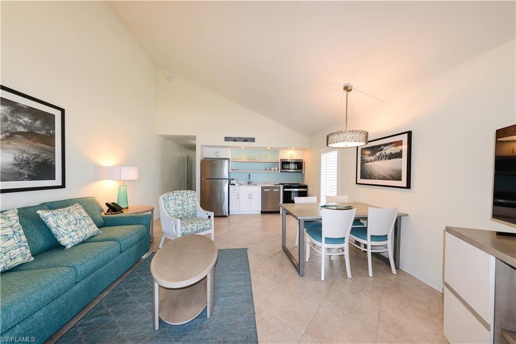 Living area with light tile patterned floors, high vaulted ceiling, bar with sink, and baseboards