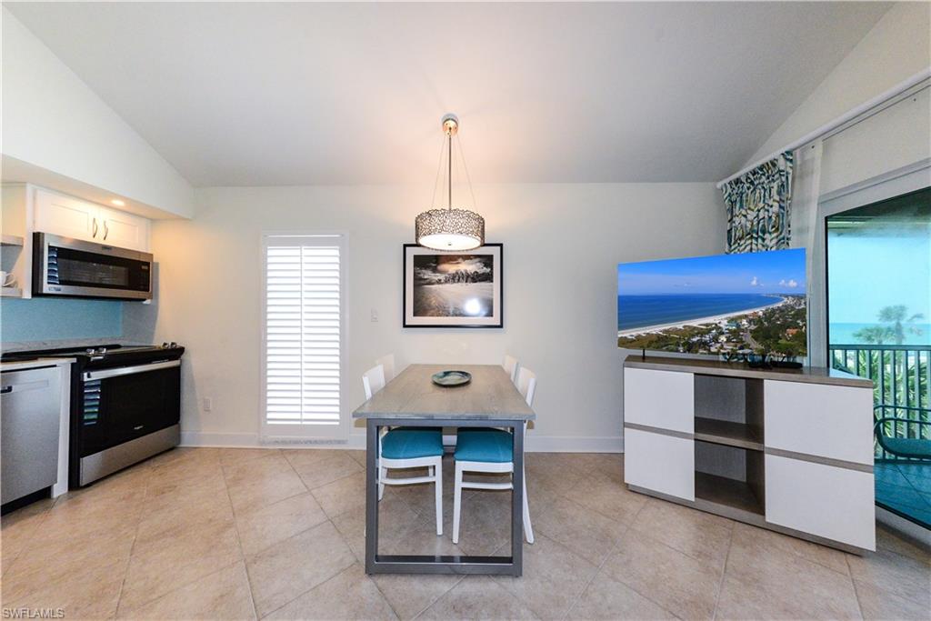 Kitchen with stainless steel appliances, vaulted ceiling, light tile patterned floors, white cabinets, and baseboards