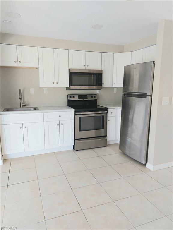 Kitchen featuring stainless steel appliances, a sink, light countertops, and white cabinetry