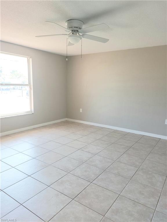 Empty room with a ceiling fan, a textured ceiling, baseboards, and light tile patterned floors