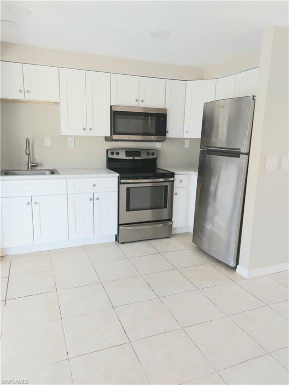 Kitchen with stainless steel appliances, a sink, white cabinetry, light countertops, and light tile patterned floors