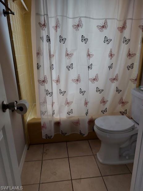Bathroom featuring toilet, shower / bath combo with shower curtain, and tile patterned flooring
