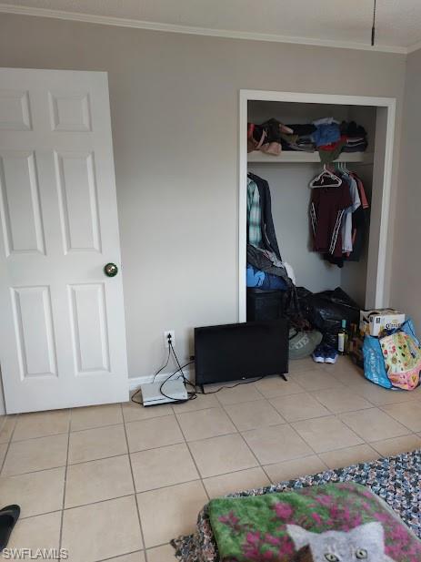 Unfurnished bedroom featuring crown molding, tile patterned floors, a closet, and baseboards