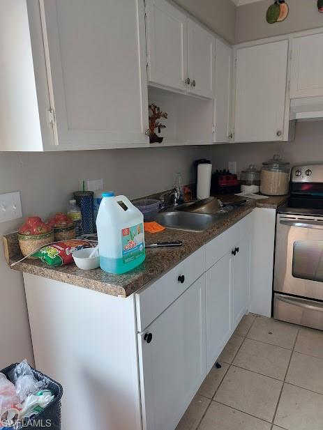 Kitchen with electric stove, a sink, under cabinet range hood, white cabinets, and light tile patterned floors