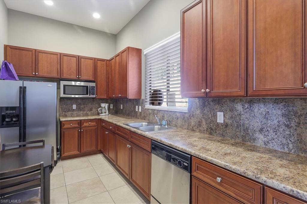 Kitchen with stainless steel appliances, a sink, light tile patterned flooring, backsplash, and light stone counters