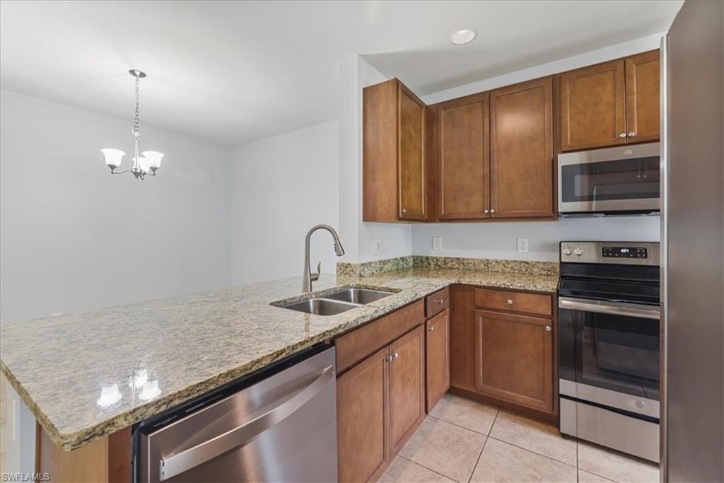 Kitchen featuring stainless steel appliances, a sink, a peninsula, light stone counters, and brown cabinets