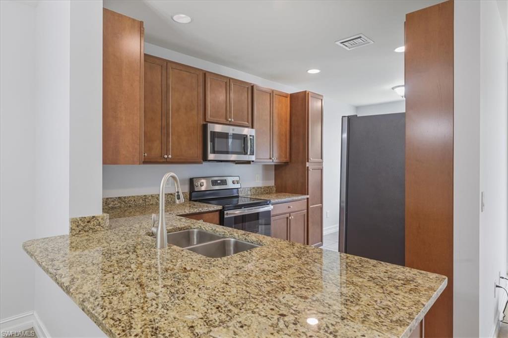 Kitchen featuring appliances with stainless steel finishes, a sink, light stone countertops, brown cabinetry, and a peninsula