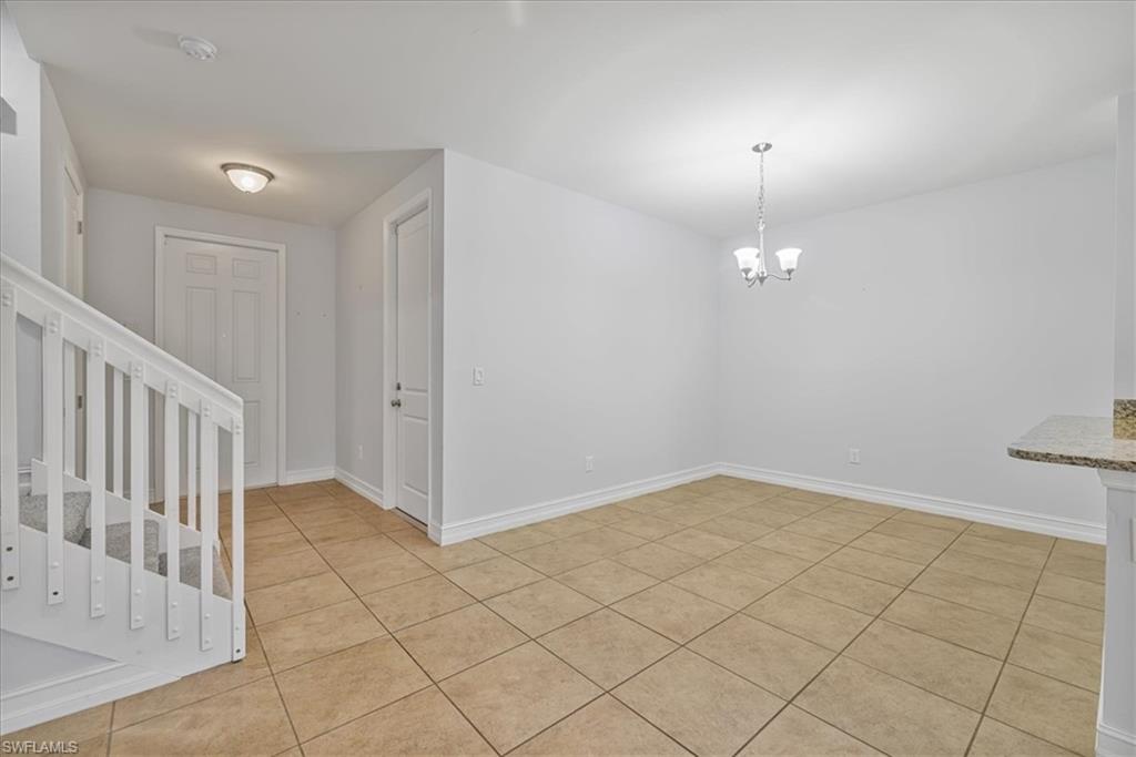 Unfurnished dining area featuring a chandelier, light tile patterned floors, baseboards, and stairway