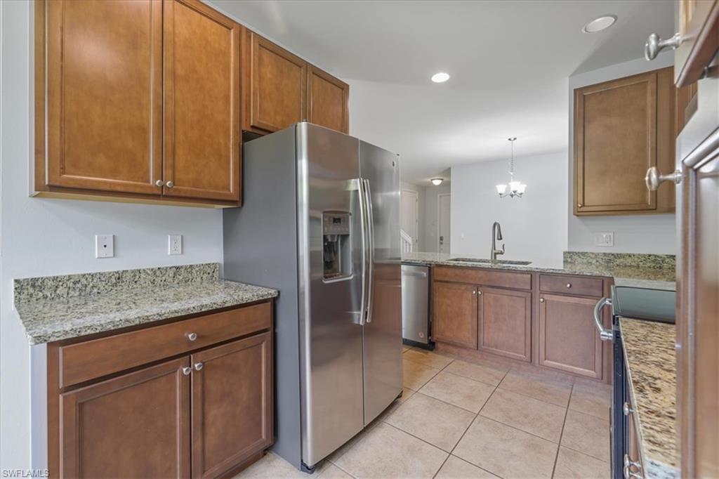 Kitchen with appliances with stainless steel finishes, a sink, light tile patterned flooring, light stone countertops, and brown cabinetry