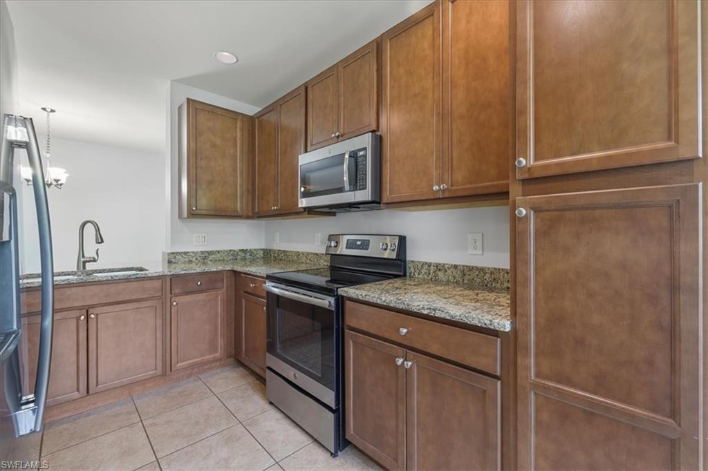 Kitchen with stainless steel appliances, light tile patterned floors, stone counters, a sink, and brown cabinets